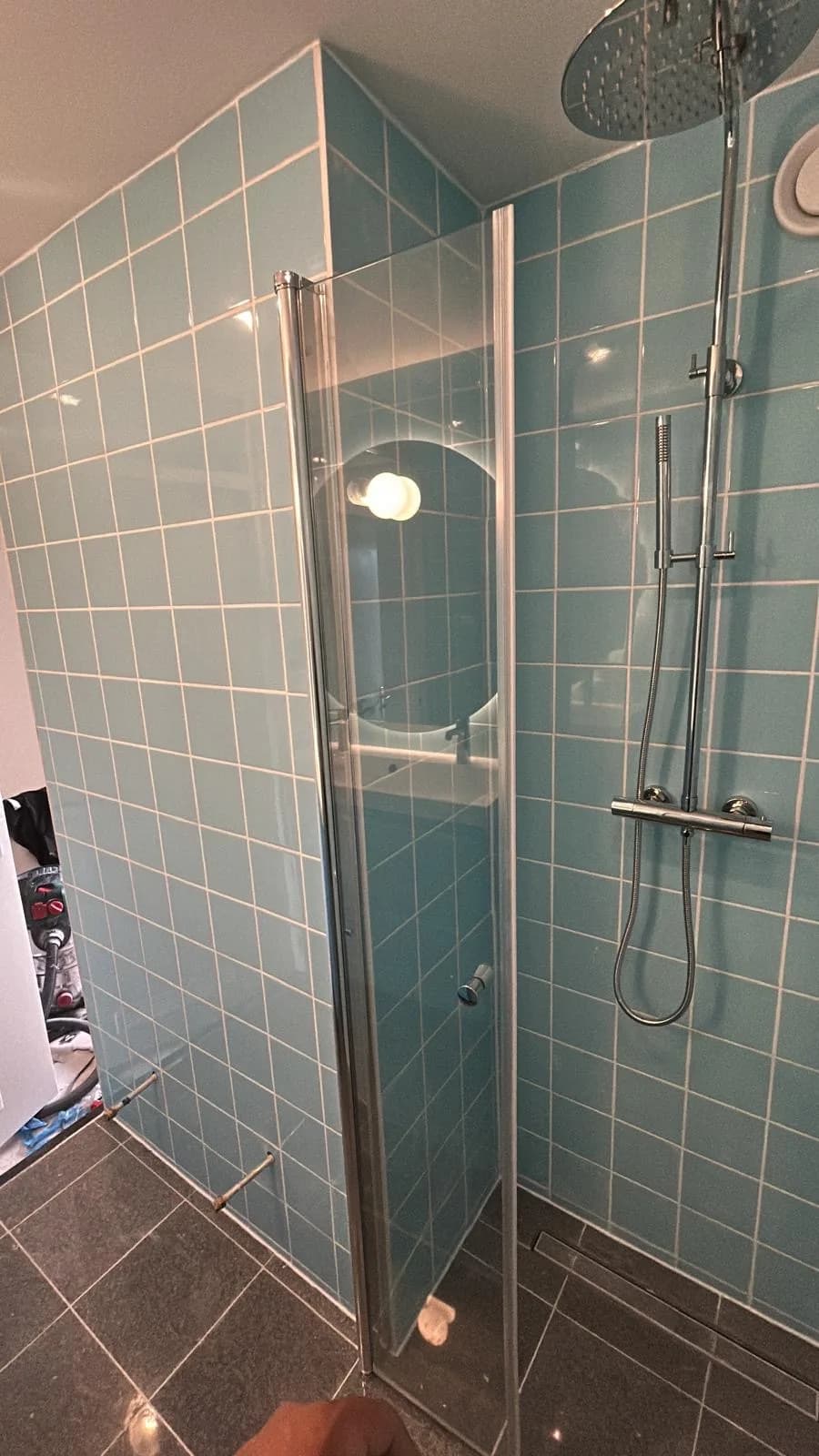 Douchehoek met glazen deur in een blauw betegelde badkamer