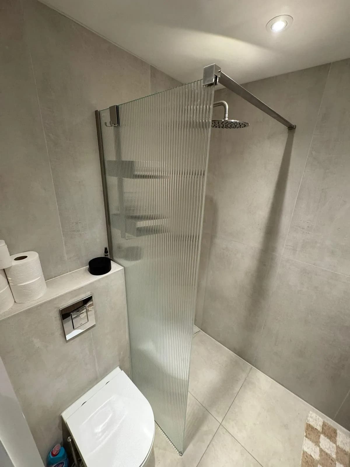 Inloopdouche met geribbeld glas en betonlook tegels in een gerenoveerde badkamer